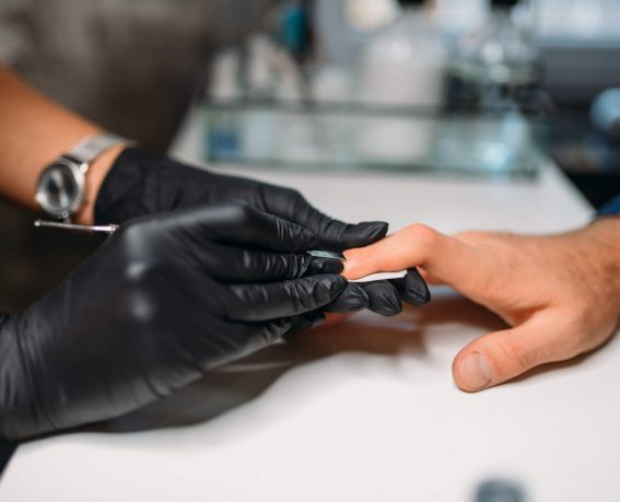 Female master in black gloves polishing nails to male client, top view, men manicure in salon. Manicurist doing hands care procedure